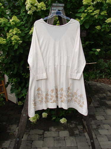 Barclay Deep V Neck Rear Banded Pocket Tunic Morning Garden Dew, size 1, features a loose fit and long sleeves, with gold-tan botanical detailing along the hem, hung on a wooden trellis.