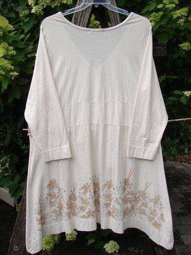 Barclay Deep V Neck Rear Banded Pocket Tunic Morning Garden Dew Size 1: A loose-fitting, cream tunic with a wide scooped neckline, three-quarter sleeves, and subtle botanical print on the hem, hanging outdoors.