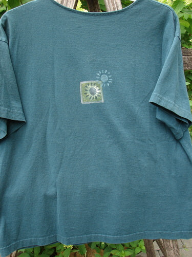 1996 Short Sleeved Promo Tee Old Frenchtown Field Viridian Size 1 draped over a wooden ladder, featuring a stylized sunflower motif on the chest, with drop shoulders and a ribbed neckline.