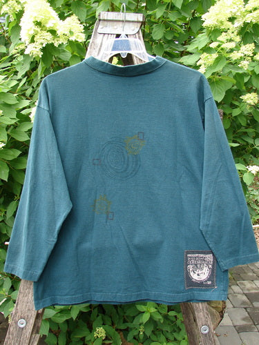 1996 Long Sleeved Tee Primitive Mask Viridian Size 1, displayed on a wooden stepladder, features drop shoulders, a ribbed neckline, and an abstract swirl graphic with colored squares, highlighting Blue Fish’s vintage creativity.