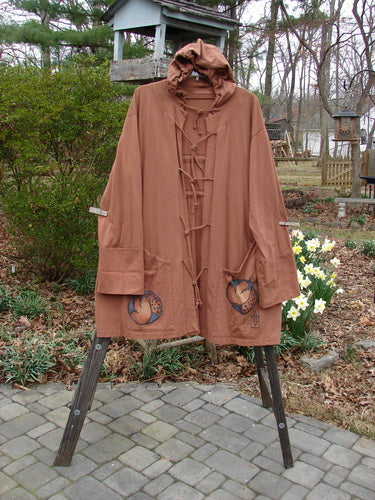 Vintage hooded jacket coat with laces on stand, outdoor setting with stone walkway and flower bed.