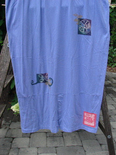 1997 Aquavella Dress Celtic Trio Skylark Size 2 displayed on a wooden rack, featuring stylized motifs in muted tones on pale lavender-blue fabric, exemplifying vintage Blue Fish Clothing's creative and individualistic style.