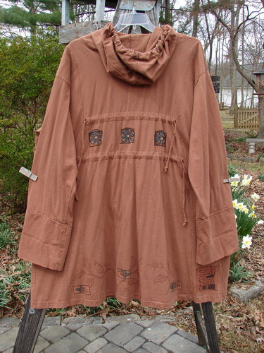 Vintage brown jacket with hood, outdoor setting, close-up of plant and stone walkway.