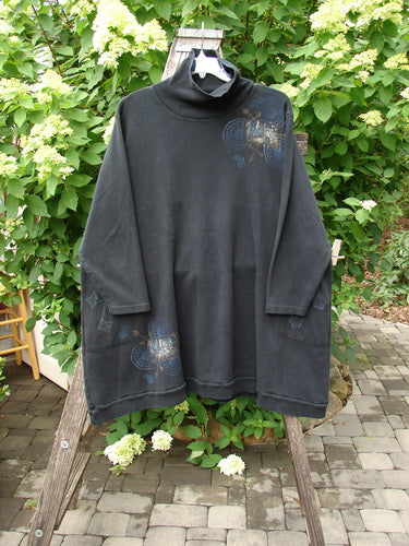Barclay Interlock Turtleneck Pullover Tunic Top Celtic Night Black Size 2, featuring a loose A-line cut, ribbed turtleneck, side pockets, and Celtic-themed motifs, displayed on a wooden ladder with a natural backdrop.