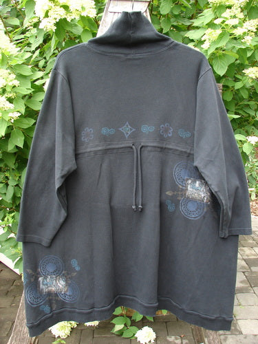 Barclay Interlock Turtleneck Pullover Tunic Top Celtic Night Black Size 2, featuring a loose fit, funnel collar, drawstring waist, and light-blue motifs, hanging outdoors against a lush foliage backdrop.