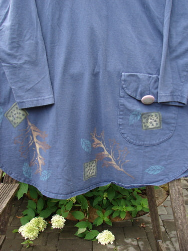 1996 Long Sleeved Pop Top Fall Leaves Niagara OSFA, a slate-blue tunic with muted gold and teal leaf motifs, features a rounded hem, scoop neckline, and oversized pocket with button, draped on an outdoor bench.