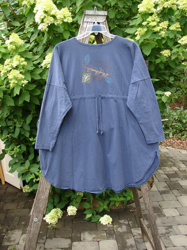 1996 Long Sleeved Pop Top Fall Leaves Niagara OSFA: A slate-blue, mid-thigh tunic with a curved hem, ¾ sleeves, drawstring waist, and subtle chest motif, displayed on a wooden ladder outdoors.