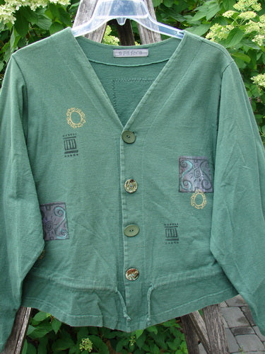 1997 Treehouse Jacket Greek Window Verdigris Size 2 features a V-neck, four-button front, decorative patches, and a drawcord flounce. Displayed outdoors, it embodies Bluefishfinder.com's vintage, expressive style.