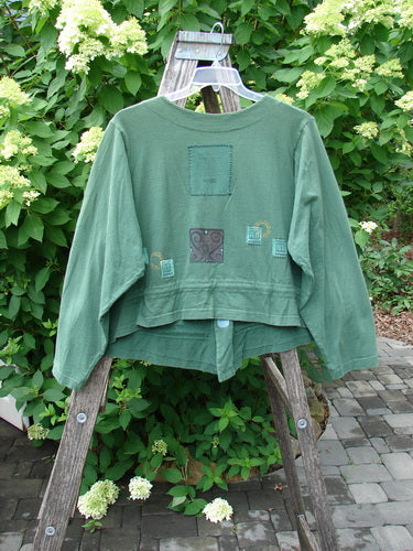 1997 Treehouse Jacket Greek Window Verdigris Size 2 displayed on a ladder, showcasing its cropped design, unique Greek Window theme, and signature Blue Fish patch against lush greenery and hydrangeas.
