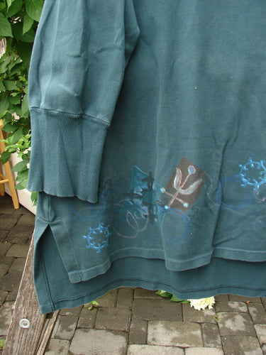 Barclay Interlock V Neck Vented Tunic Top Celtic Tumble Forest Teal Size 2 features stylized bicycle wheels and snowflake motifs, draped over a bench, showcasing its unique design and longer A-line shape.