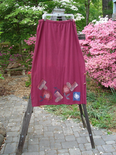 Barclay Panel Nut Button Vented Skirt Oakleaf Madder Size 2: A straight skirt with tall vented sides and nut-like buttons. Features a larger elastic waistline and leaf-themed paint around the hemline.