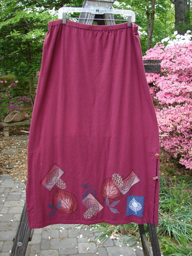 Barclay Panel Nut Button Vented Skirt Oakleaf Madder Size 2: A straight skirt with tall vented sides, nut-like buttons, and a leaf theme paint around the hemline. Made from medium weight organic cotton.