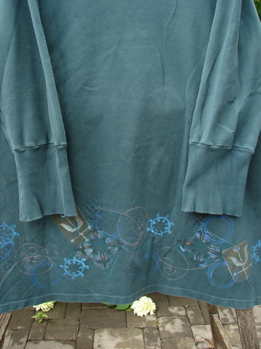 Barclay Interlock V Neck Vented Tunic Top Celtic Tumble Forest Teal Size 2, featuring a heavy ribbed neckline, interlocking gear graphics, shirttail hemline, and vented sides, draped on a brick surface.