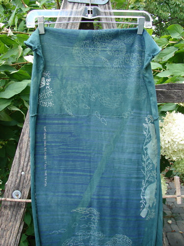 Barclay Wide Sectional Scarf Wrap Forest Animals Mottled Green OSFA, featuring enchanting forest animal motifs and motivational quotes on a lightweight teal fabric with finished curly edges, hanging gracefully outdoors.