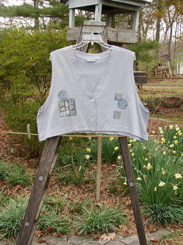 1994 Spruance Vest Topiary Solstice Blue OSFA displayed on a wooden rack, featuring a generous rear paint with topiary design, dual paper button closure, and wide A-line flare.