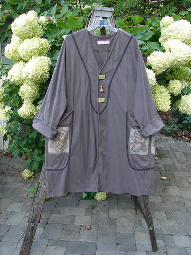 1998 Tiddly Winks Jacket Butterfly Madeira Size 2: A loose-fitting grayish-taupe tunic with three-quarter sleeves, decorative toggle buttons, patterned pockets, and piped trim, hanging on a wooden frame.