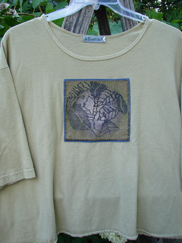 Barclay PMU Patched Short Sleeved Crop A Lined Tee Honey Size 2, featuring a loose fit, three-quarter sleeves, and a central abstract botanical patch, hanging on a tree limb outdoors.