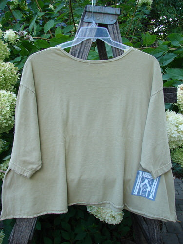 Barclay PMU Patched Short Sleeved Crop A Lined Tee Honey Size 2, featuring a loose-fit, olive-green design with a small fabric patch on the hem, displayed on a rustic wooden A-frame.