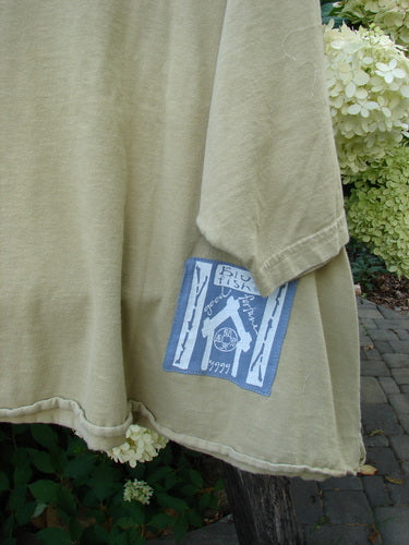 Barclay PMU Patched Short Sleeved Crop A Lined Tee features a muted green-beige tone with a pale blue and white patch depicting birch trunks and a stylized fish, showcasing Bluefishfinder's upcycled vintage style.