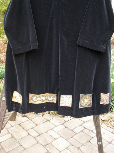 1999 Velveteen Poet's Coat Holiday Celtic Black Size 1: A black coat with gold designs, oversized vintage buttons, folded collar, and two front floppy pockets, featuring colorful patches and a varying hemline.