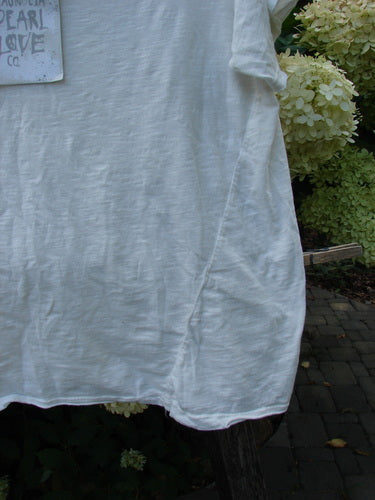 The Magnolia Pearl NWT Cotton Europa V Neck Boyfriend Tee True White OSFA is draped over a wooden ladder, showcasing its raw edges, hand distressing, and feminine V neckline against a garden background.