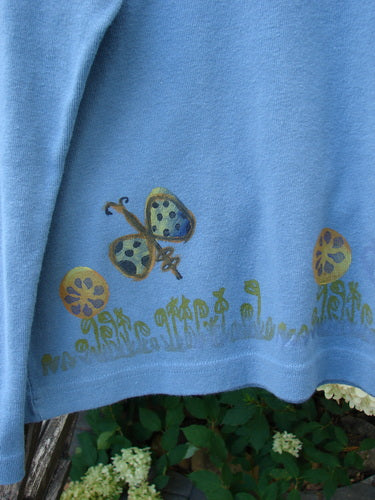 1999 Round Neck Rib Top Butterfly Blue Stone Size 2 features a painted butterfly and floral design on the hem, draped over a railing, showcasing its ribbed fabric and flared hemline.
