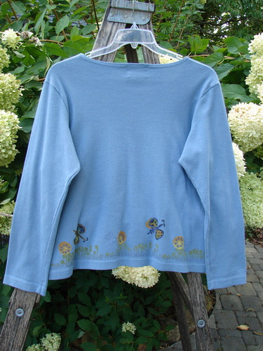 1999 Round Neck Rib Top Butterfly Blue Stone Size 2 hangs on a ladder, showcasing its ribbed, slightly cropped boxy shape, flared hem, and whimsical mushroom and fairy design along the hem.