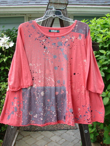 A pink shirt with paint splatters on a swing, featuring a textured A-lined shape, rounded neckline, and curly edgings. Size 2.
