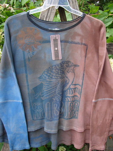 Barclay NWT Thermal Crop Top Finch Mottled Bibbi Blue OSFA, featuring a gradient bird graphic, scoop neckline, and drop shoulders, displayed outdoors on a hanger against lush greenery.