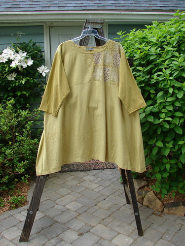A mustard yellow hemp linen dress with cotton sleeves, featuring a sectional upper and a pleated A-line shape. The dress has a slightly shallow rounded neckline and a cobblestone corner stone theme paint. Size 2.