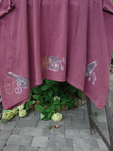 1994 Short Simple Smock Magic Music Beet Size 2 displayed draped on wood, features hand-painted musical motifs, rounded neckline, sectional panels, and varying hemline, embodying Blue Fish Clothing's unique vintage style.