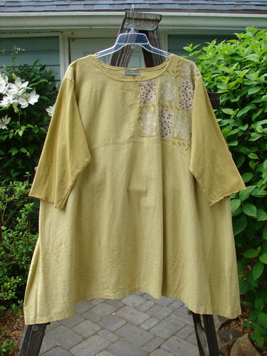 A mustard yellow dress with patchwork design on the sleeves. Sectional upper with a curved empire waist seam and pleated A-line shape. Three-quarter length contrasting cotton sleeves. Cobblestone corner stone theme paint. Size 2.