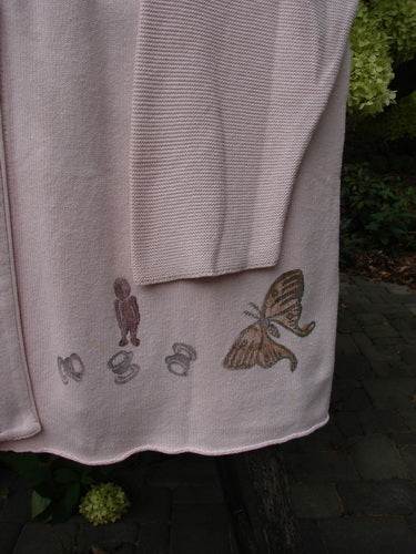 Pale-pink woven textile with embroidered motifs, showcasing the 1994 2 Button Cardigan Sweater Magical Garden Pink Granite OSFA, highlighting its unique stitch patterns and oversized design amidst a natural outdoor setting.