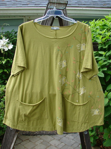 A Barclay Double Pocket Twinkle Top in Peapod, featuring a green shirt with birds on it. A-line shape, scalloped hemline, and lower exterior pockets.