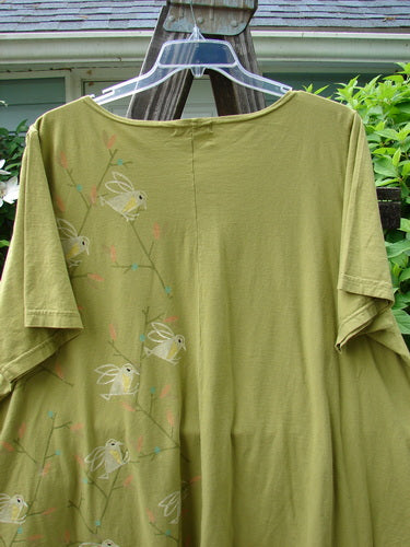 A Barclay Double Pocket Twinkle Top in Peapod, featuring a song bird theme paint. A-line shape, scalloped hemline, and lower exterior pockets. Made from medium weight organic cotton.