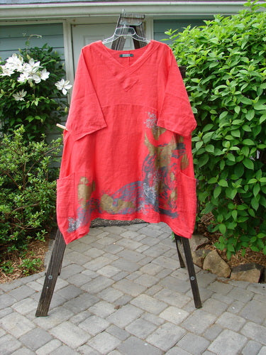 A red Barclay Linen Cross Over Dress with a nifty cross over front V neckline, drop shoulders, and a downward curved empire waist seam, showcased on a clothes rack.