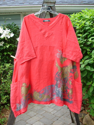 A red shirt with a deer design on it, part of the Barclay Linen Cross Over Dress Golden Lookout Geranium Size 2 collection. Features a cross over front V neckline, drop shoulders, and a downward curved empire waist seam. Varying side lengths and double drop flop side pockets. Made from medium weight linen.