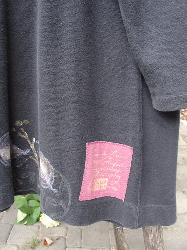 1998 Heavy Berber Kindlewood Tunic Leaf Sprig Black OSFA, featuring a dark charcoal-gray knit with an A-line shape, pink fabric patch, abstract vine motif, and cozy long sleeves hanging outdoors.
