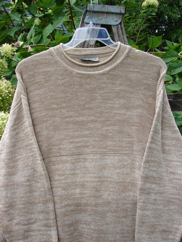 Barclay Jennifer's Rollneck Sweater Marled Aspen OSFA, a beige knit sweater with a rolled hem and textured knits, elegantly displayed on a hanger against lush foliage and blooming hydrangeas.
