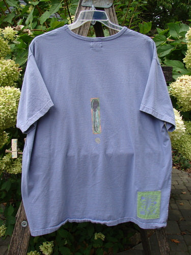1999 Short Sleeved Tee Reverse Heart Vase Iris Size 2, showcasing a unique exclamation mark design and square print, elegantly draped on a trellis with hydrangeas, highlighting its vintage Blue Fish style.