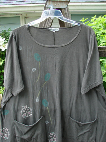 A grey Barclay Double Pocket Twinkle Top with ladybug theme paint. Features include a ruffle hem, banded lower sleeves, and double drop pockets. Made from medium weight organic cotton.