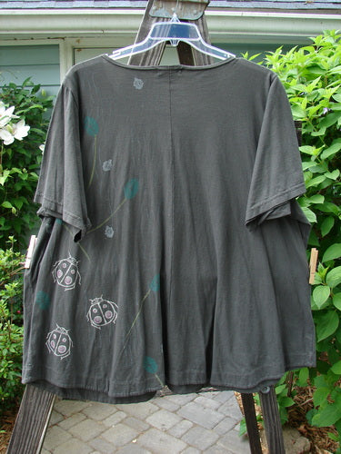 Barclay Double Pocket Twinkle Top Ladybug Grey Hunter: A medium weight organic cotton shirt with ladybugs painted on it. Features include a ruffle hem, banded lower sleeves, double drop pockets, and an A-line shape.