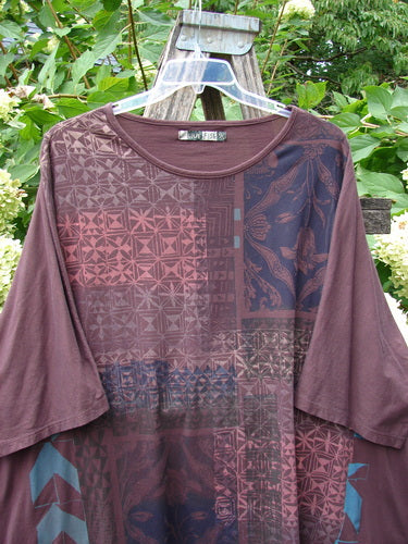 Barclay Art Tee Grid Flower Lower Lily Red Plum OSFA: Loose-fitting brown top with geometric and floral patchwork, rounded neckline, and varying hemline, highlighting its artistic design against a backdrop of lush greenery.