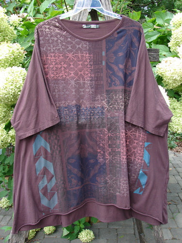 Barclay Art Tee Grid Flower Lower Lily Red Plum OSFA hanging outdoors, showcasing its loose cut with patchwork-style geometric and floral motifs, three-quarter sleeves, and rounded neckline.