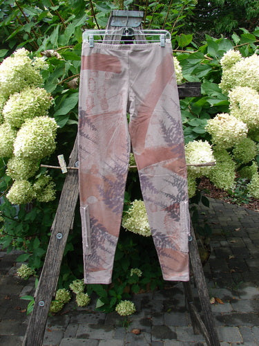 Barclay NWT Cotton Lycra Side Gather Drawcord Legging Forest Moon Oriel Size 1, featuring a camouflage pattern with muted tones, hanging on a wooden A-frame against lush greenery and hydrangeas.