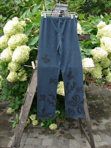 Barclay NWT Cotton Lycra Straight Pant Botanicals Lux Silhouette Size 1, featuring a black stencil-style botanical motif on the lower legs and thigh, displayed on a wooden garden ladder.