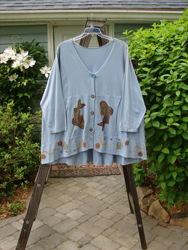 1993 Modernismo Cardigan Koi Periwinkle OSFA: A blue cardigan with a koi pond theme paint, old time buttons, drop and curved kangaroo tunnels, and a wide rounded swing. Features a drawcord back, oversized signature patch, and a banded hemline.