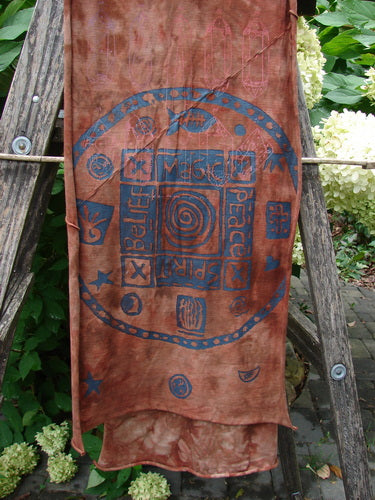 Barclay Diagonal Scarf Wrap Belief Spirit Magic Mottled Rust OSFA draped on a wooden ladder in a garden, showcasing a circular mandala with Magic, Peace, Spirit, Belief symbols on organic cotton.