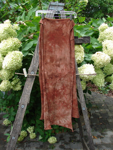 Barclay Diagonal Scarf Wrap Belief Spirit Magic Mottled Rust OSFA draped over a wooden ladder, showcasing its sweet raw curly edges and exterior diagonal seams against a lush green backdrop.