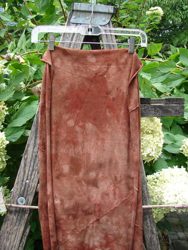 Barclay Diagonal Scarf Wrap Belief Spirit Magic Mottled Rust OSFA: A medium-weight organic cotton wrap with raw curly edges and diagonal seams, displayed on a clear hanger against a rustic ladder backdrop.